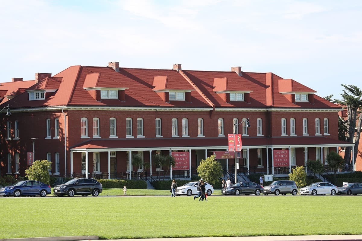A long pale brick building with a flag, seen from a lawn