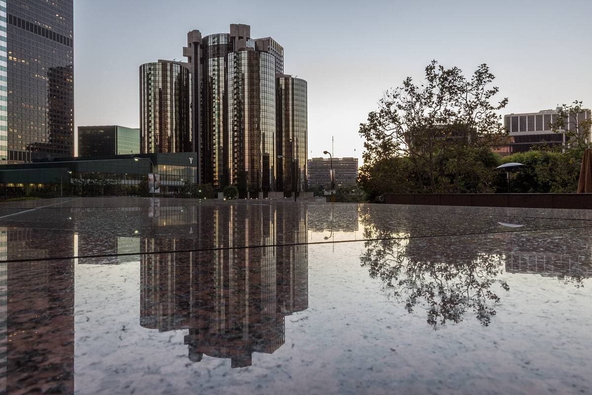 Five cylindrical glass towers reflected in a wet plaza at dusk