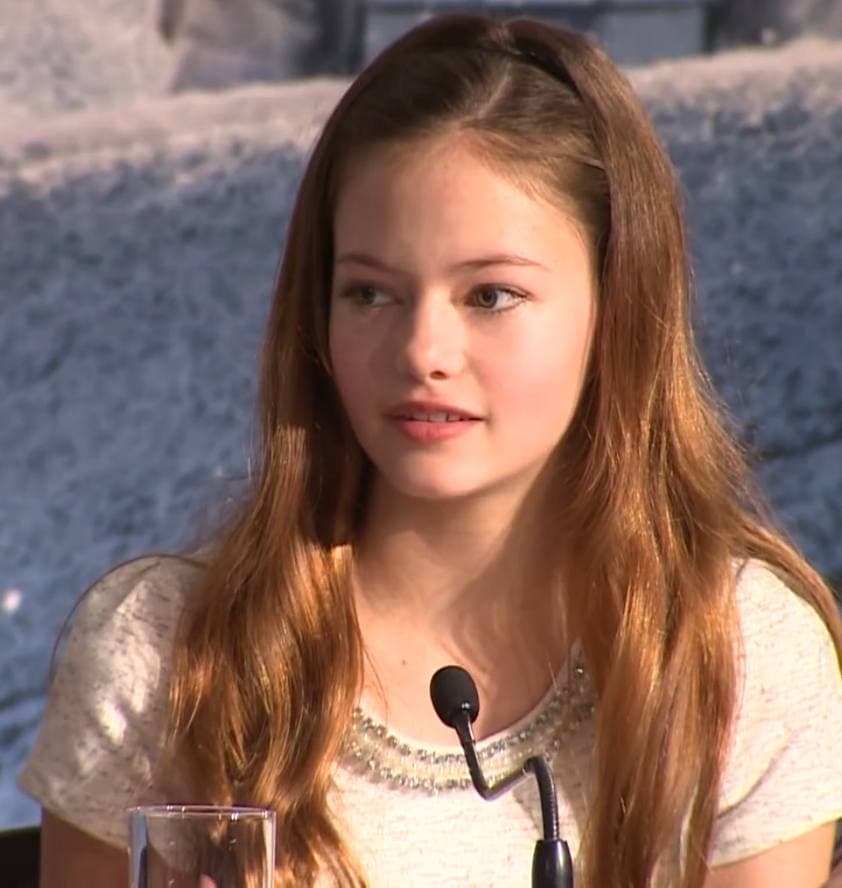 Mackenzie Foy with long brown hair speaking at a press conference microphone