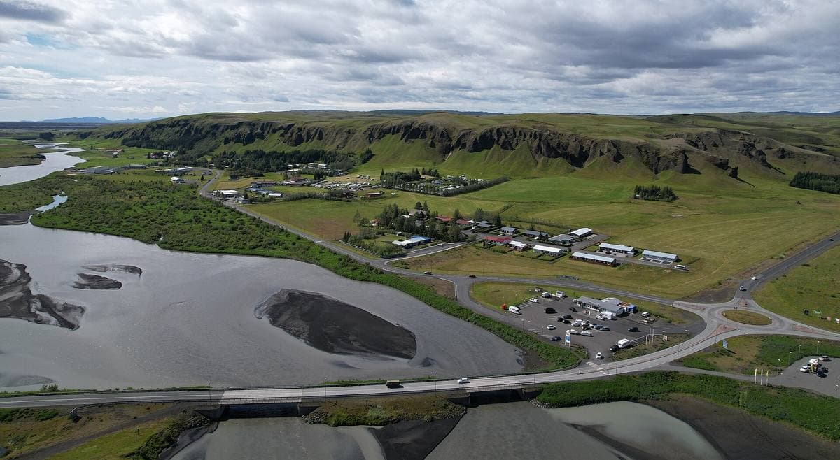 Aerial view of a small village beside a braided grey river and green cliffs
