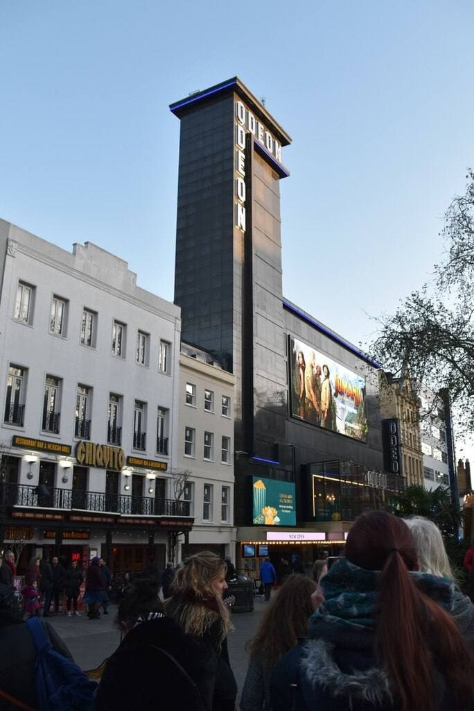 A tall dark cinema tower over a London square at dusk