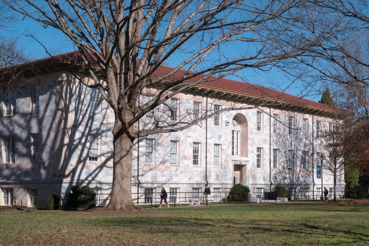 A white marble university building with a red tile roof behind a bare tree