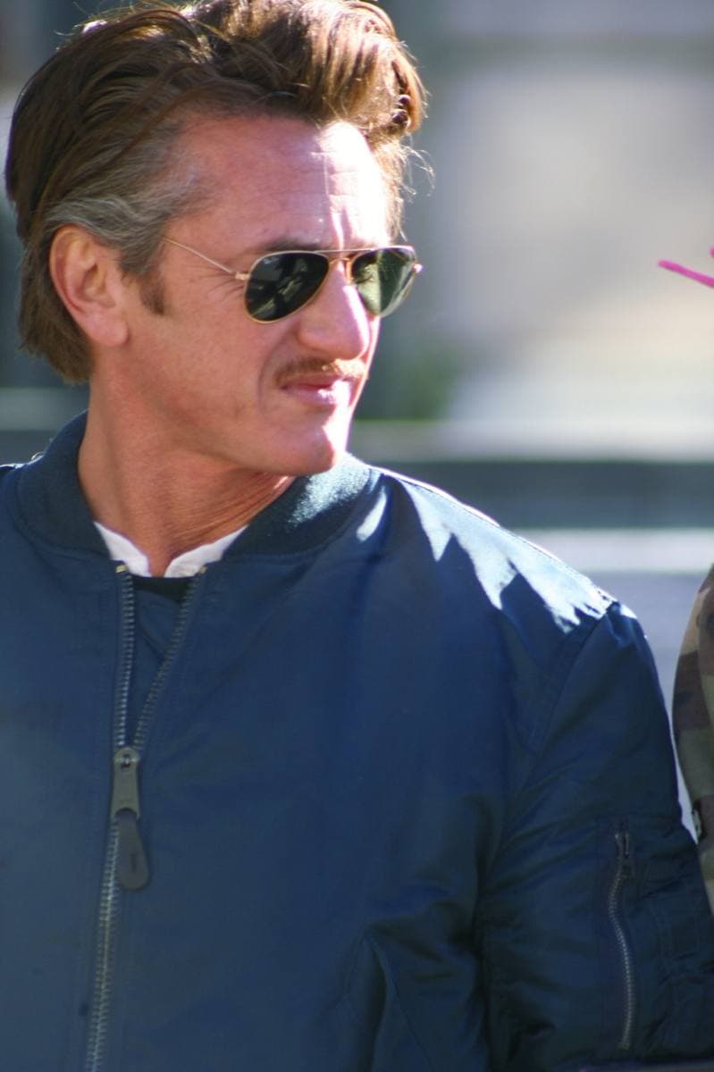 Sean Penn in sunglasses and a navy bomber jacket, in profile outdoors
