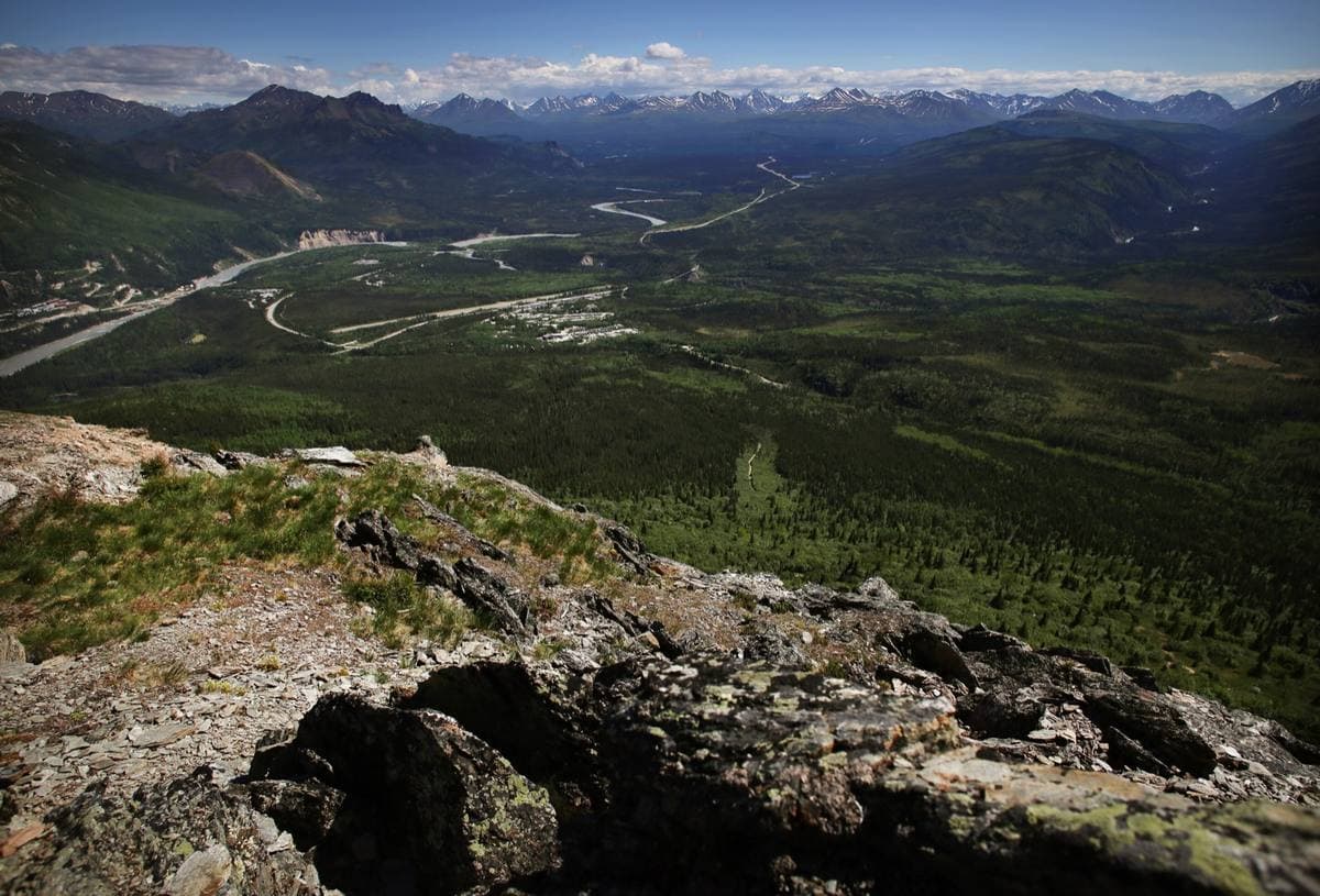 A highway and a braided river running through a wide green valley between mountains