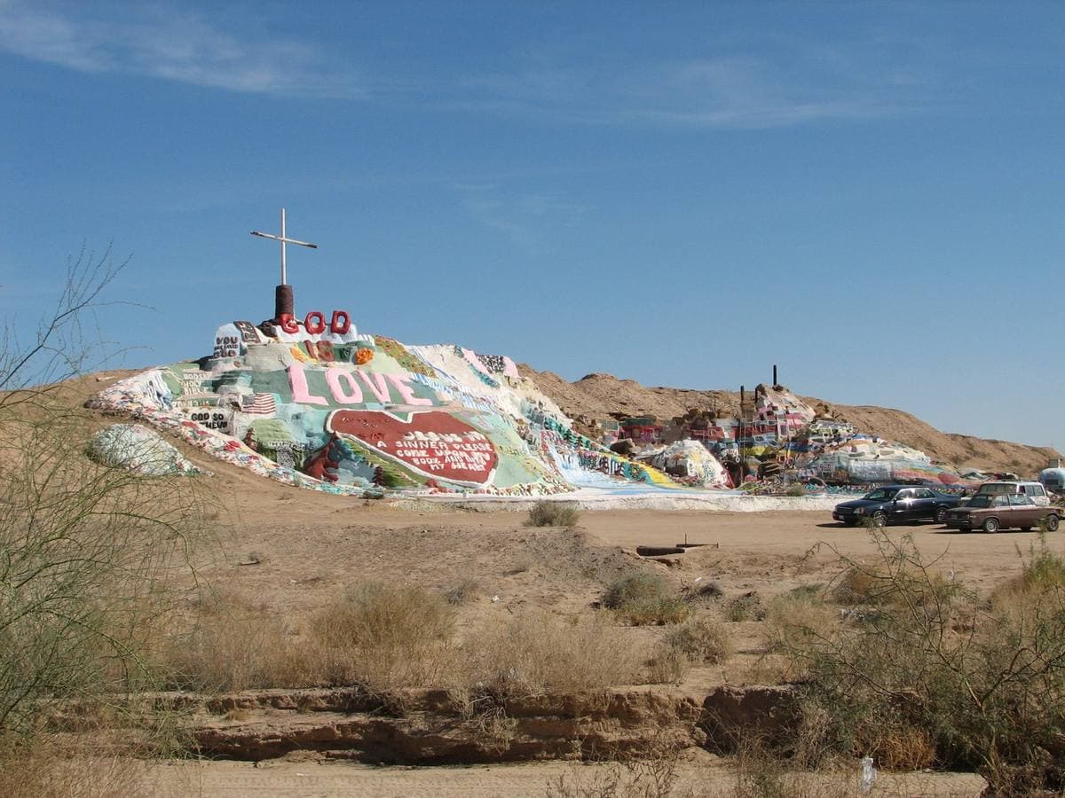 The painted hill from a distance across dry desert scrub, cars parked at its foot