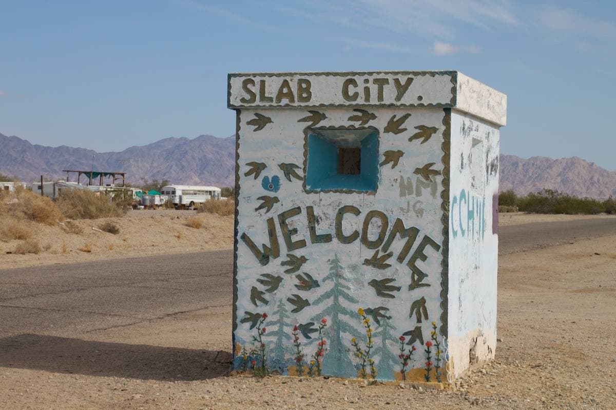 A concrete guard post painted with the words Slab City and Welcome, desert behind