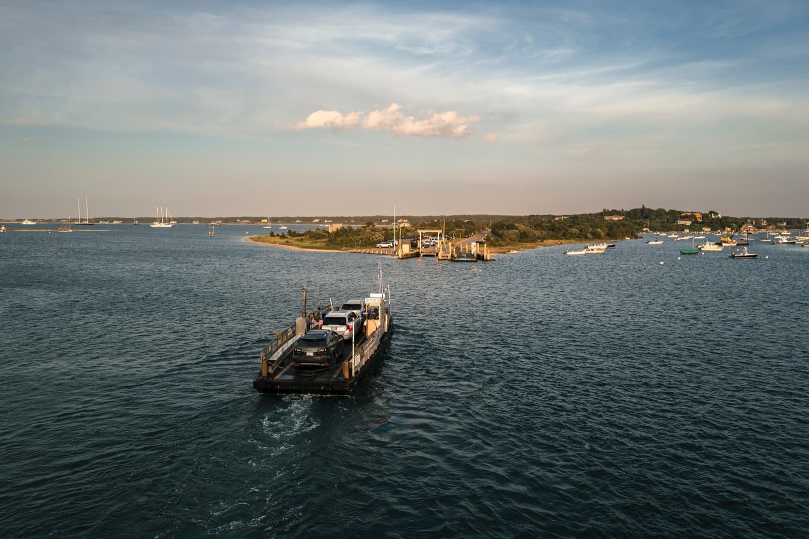 A small flat ferry carrying cars across the harbour at dusk