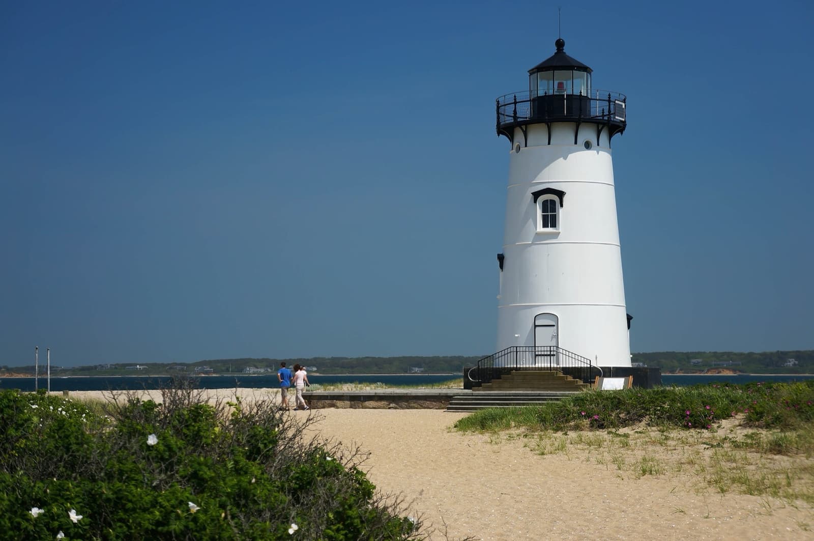 A white lighthouse on a sandy point under a deep blue sky