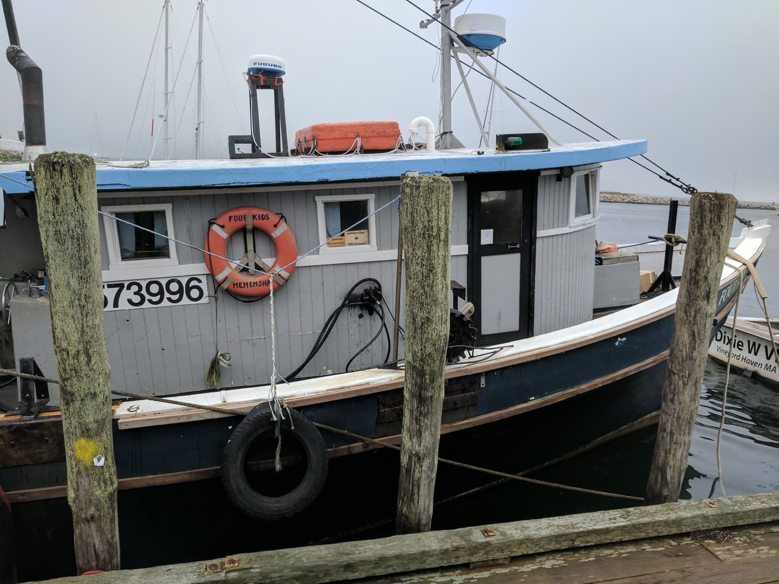 A white wooden fishing boat with a life ring tied up between dock posts