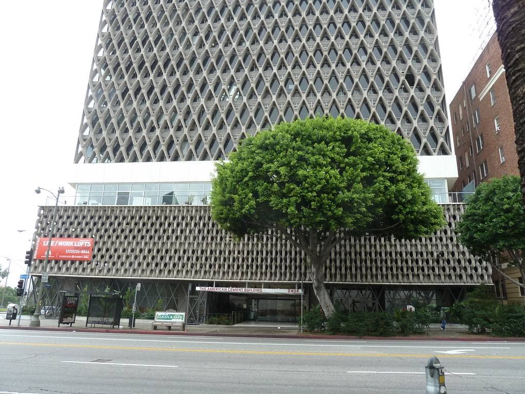 A tall concrete building wrapped in a lattice of X shapes above a street with a tree