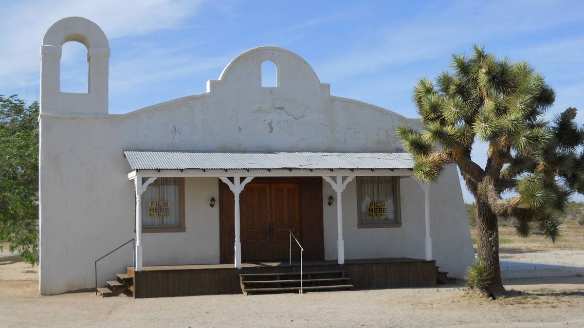 A small white Spanish-style chapel with a bell gable and a Joshua tree beside it