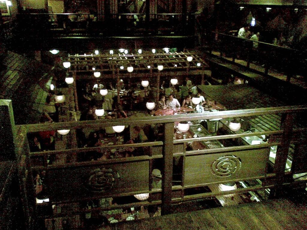 Rows of round white lanterns hanging over the tables of a busy timber hall, seen from above