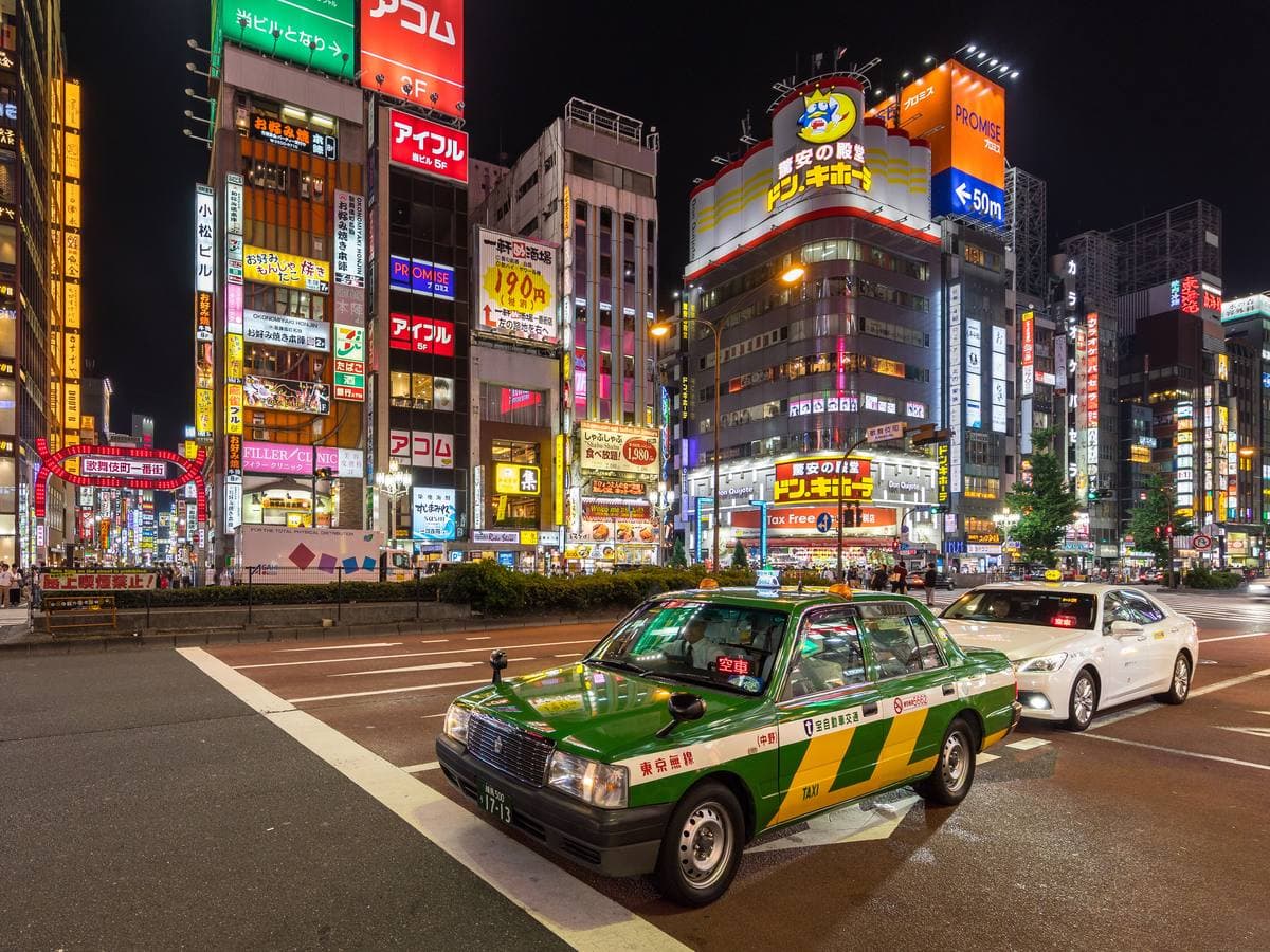 A green and yellow taxi on Yasukuni-dori at night under walls of neon signs