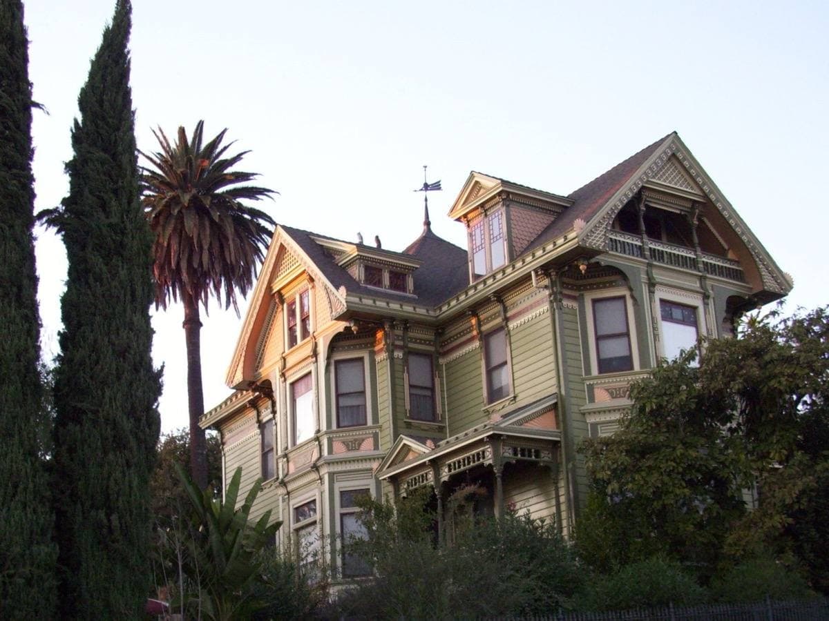 A painted Victorian house with a turret, palms and a cypress