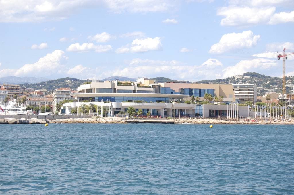 A long low white festival hall on the Cannes waterfront, hills behind