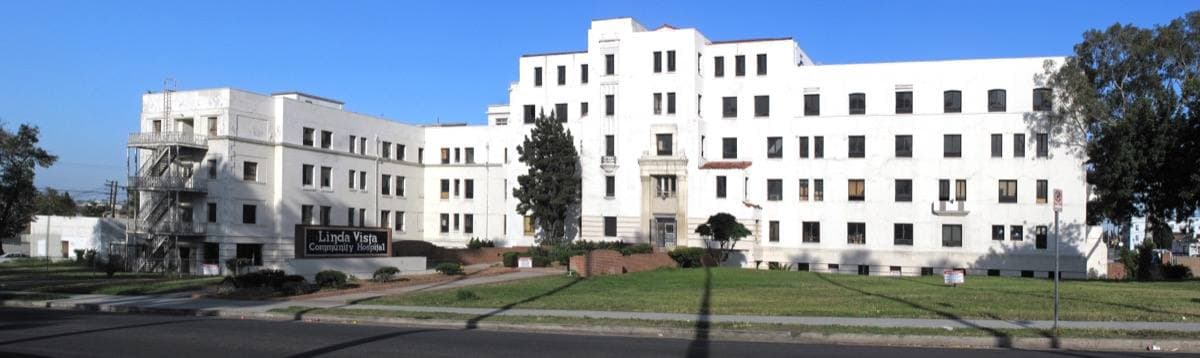A long white Mission Revival hospital building behind a lawn