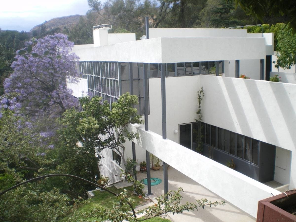 A white modernist house of stacked balconies behind purple jacaranda