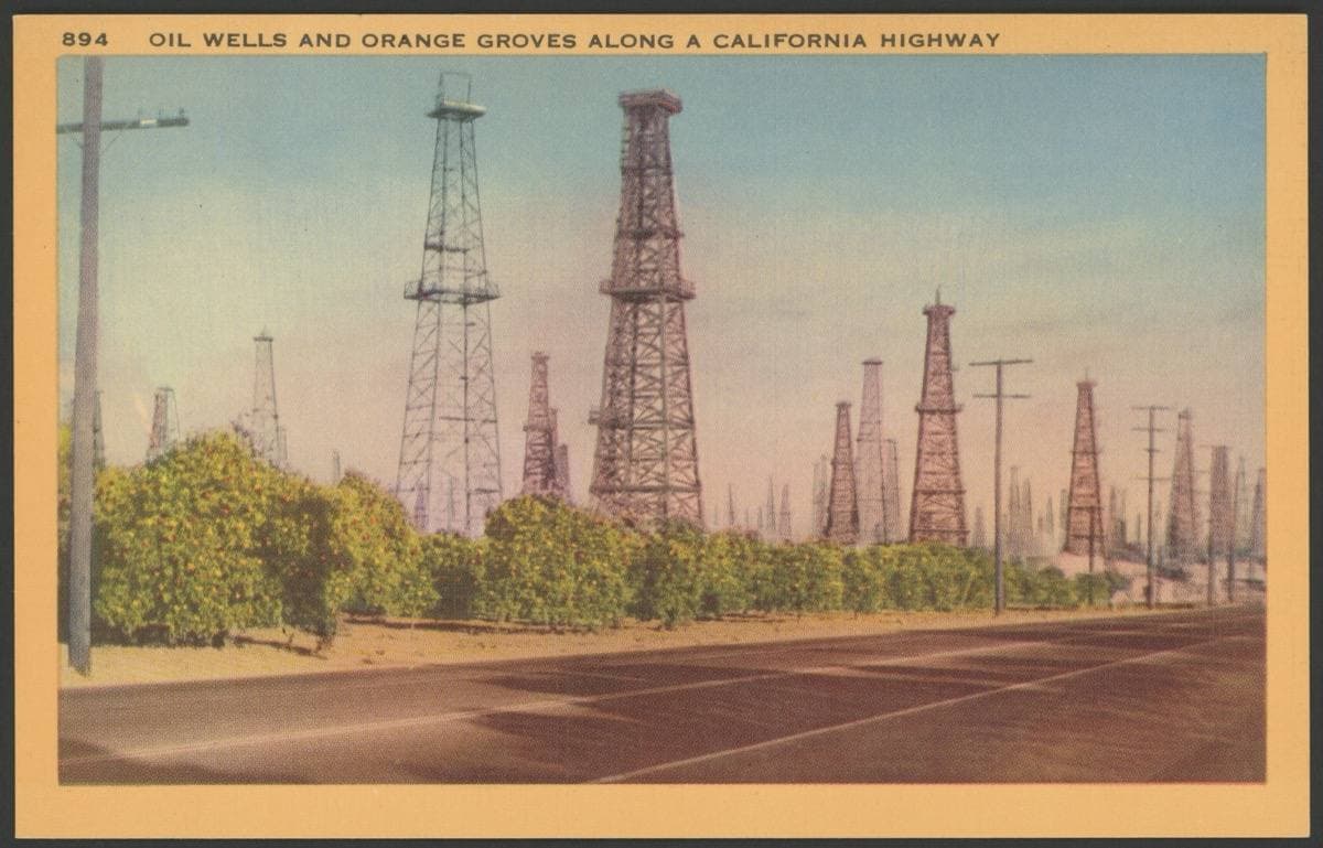 A tinted postcard of oil derricks rising behind orange groves by a highway