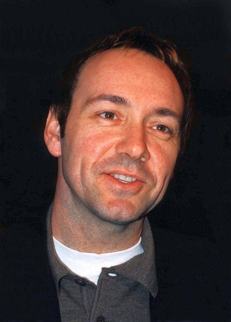 Kevin Spacey smiling, in an open-necked grey shirt