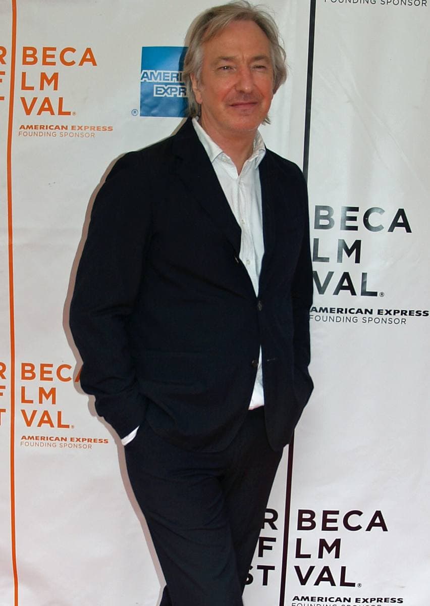 Alan Rickman in a dark suit, hands in pockets, in front of a festival backdrop