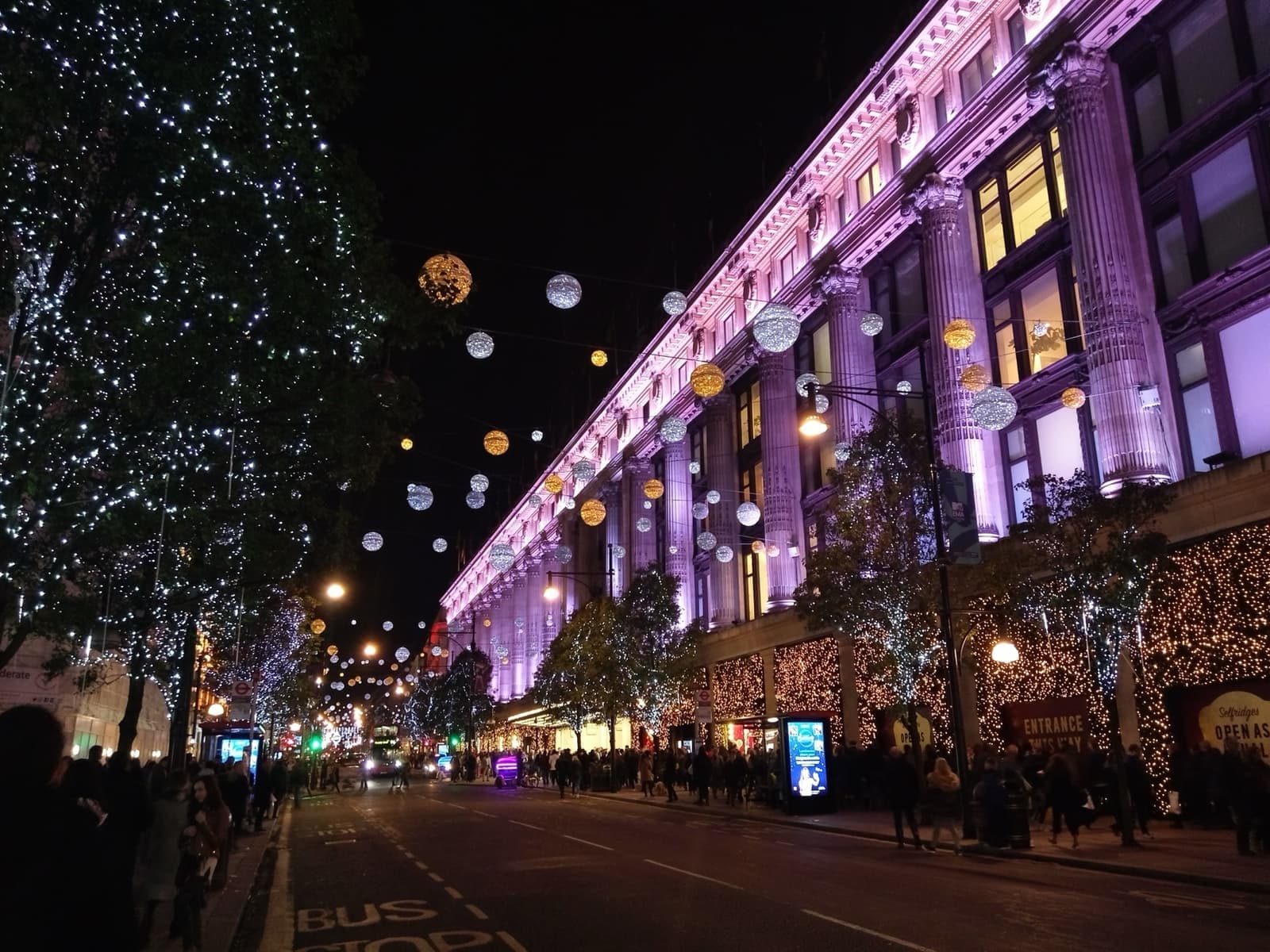 Selfridges lit purple at night with Christmas lights strung over Oxford Street
