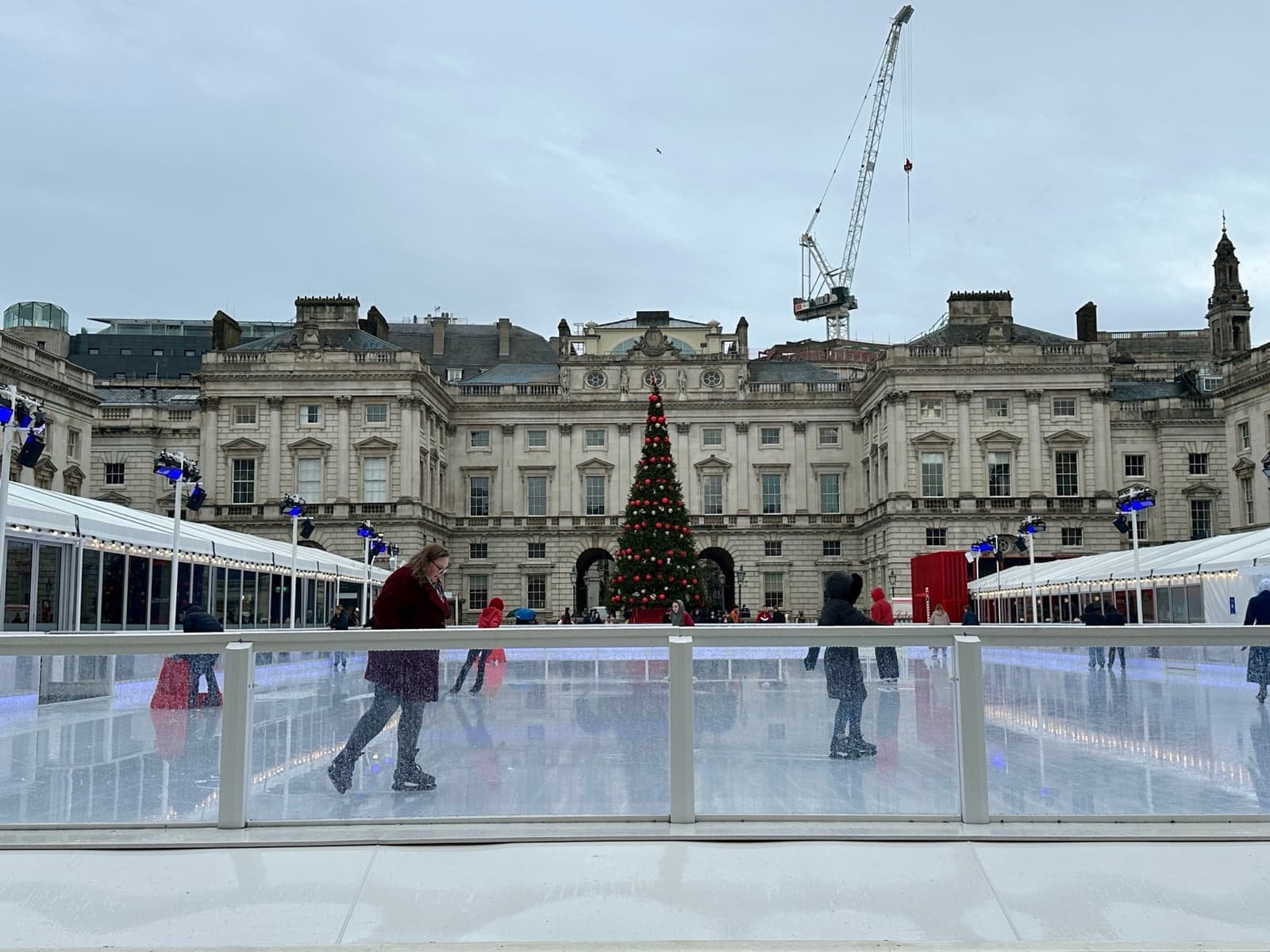 Skaters on the ice rink in the Somerset House courtyard with a lit Christmas tree behind