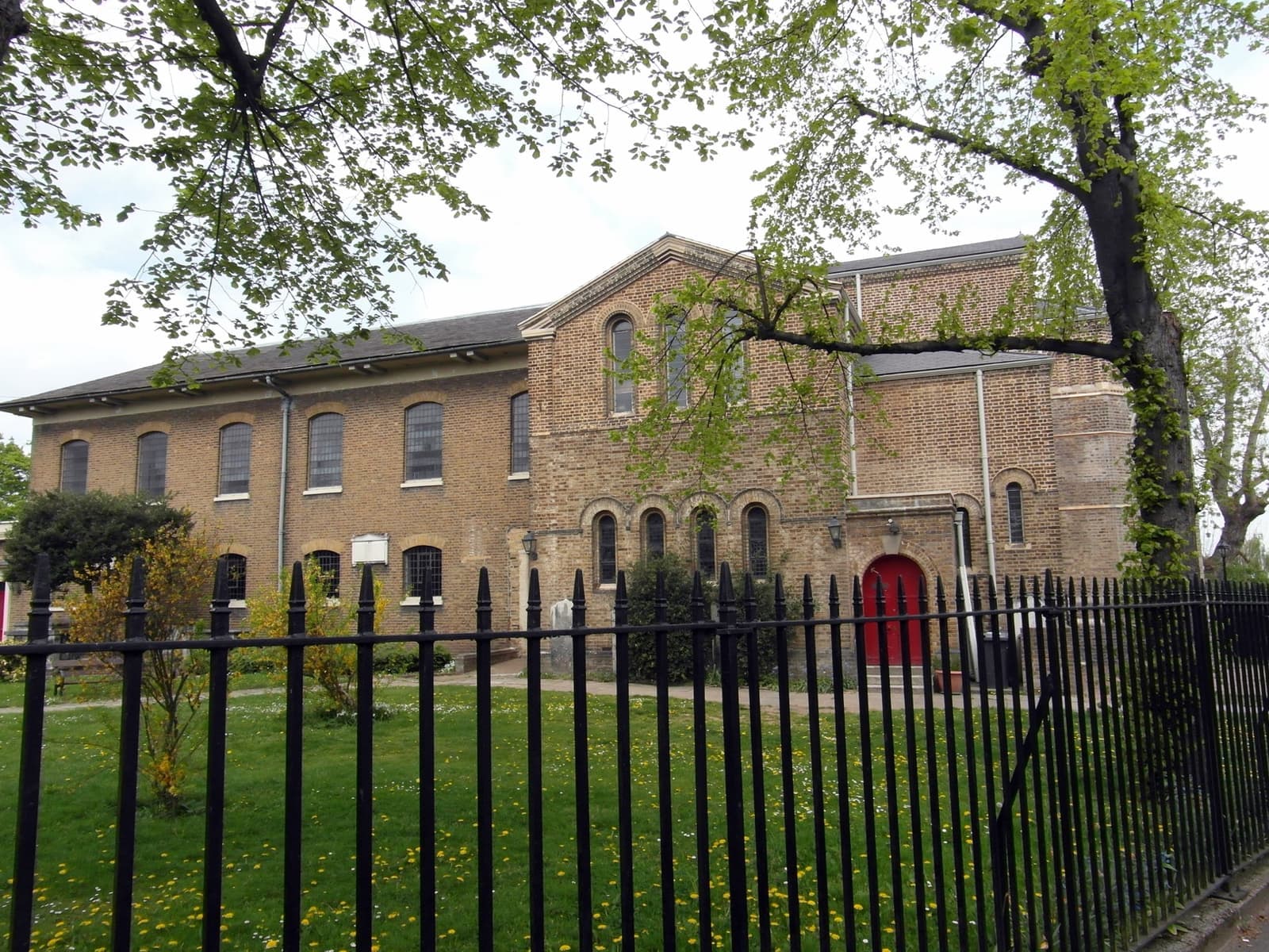 A brick church behind railings and a green churchyard