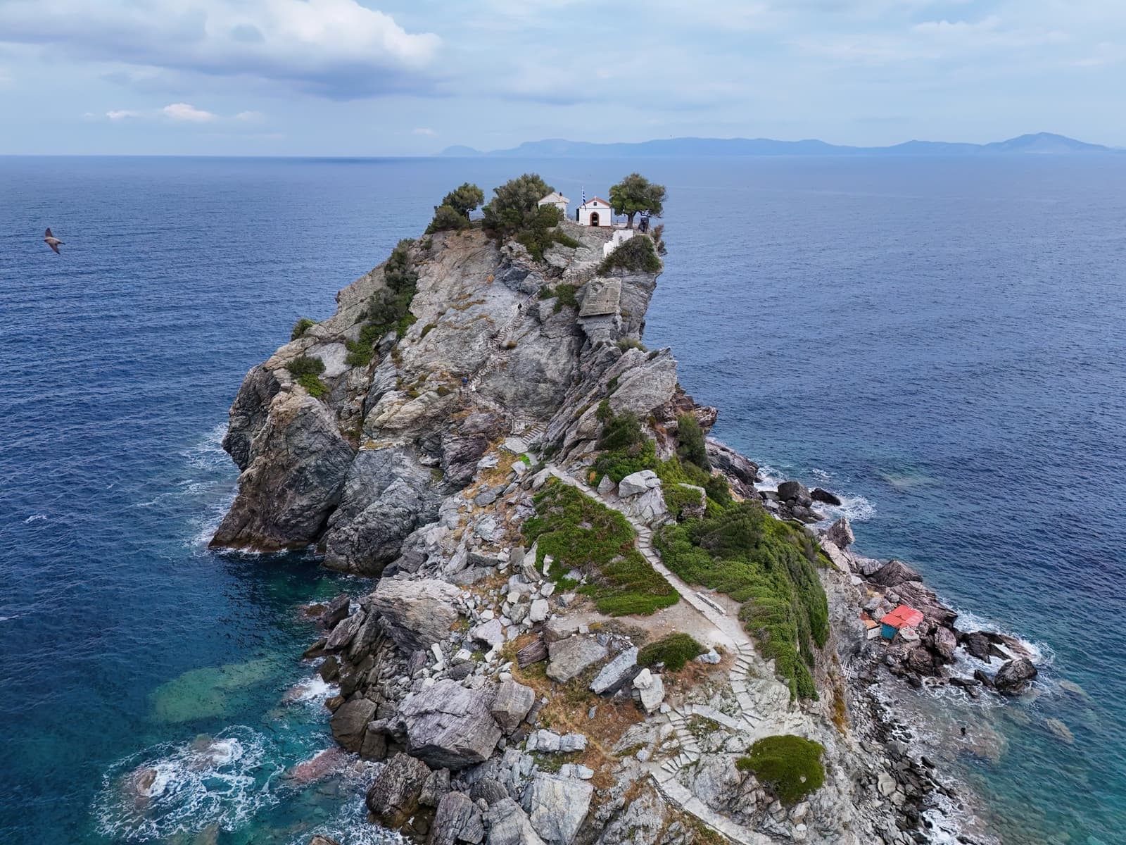 A small white chapel on top of a steep green rock rising out of a dark blue sea