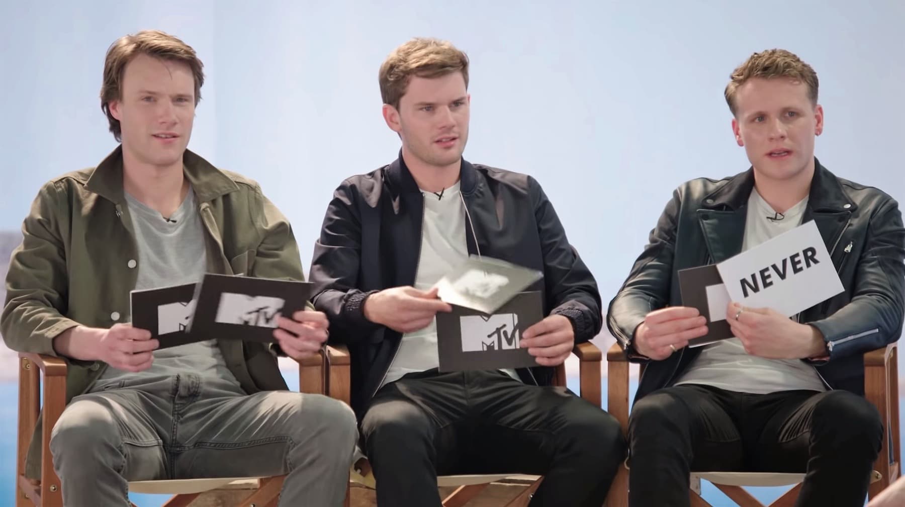 Three young men sitting on director’s chairs holding cards
