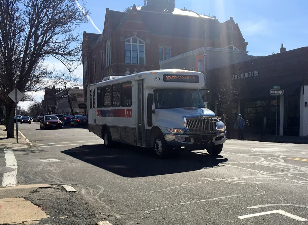 A small shuttle bus on a town street lined with shops