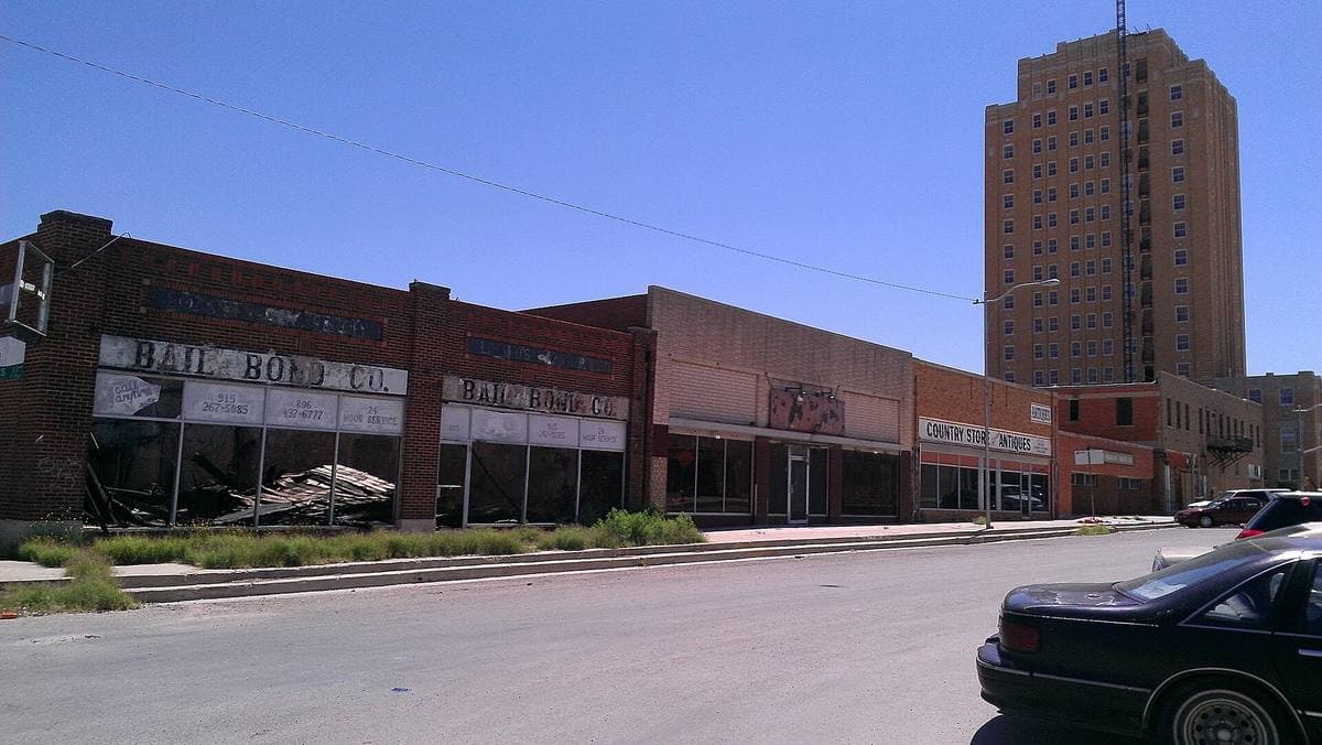 A row of closed brick shopfronts on a wide empty street, the hotel tower behind
