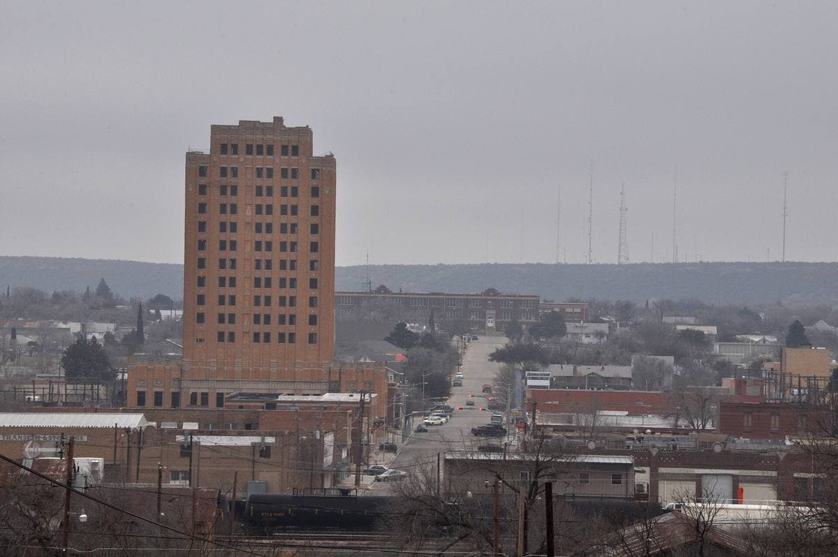 A tall brick hotel tower above a low West Texas town under a grey sky