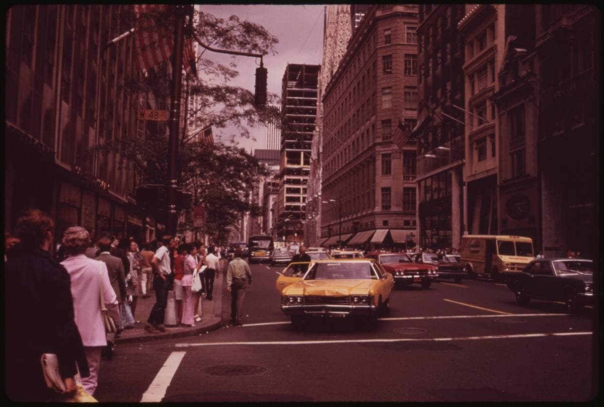 A yellow cab angled across a crossing on Fifth Avenue, people crossing behind
