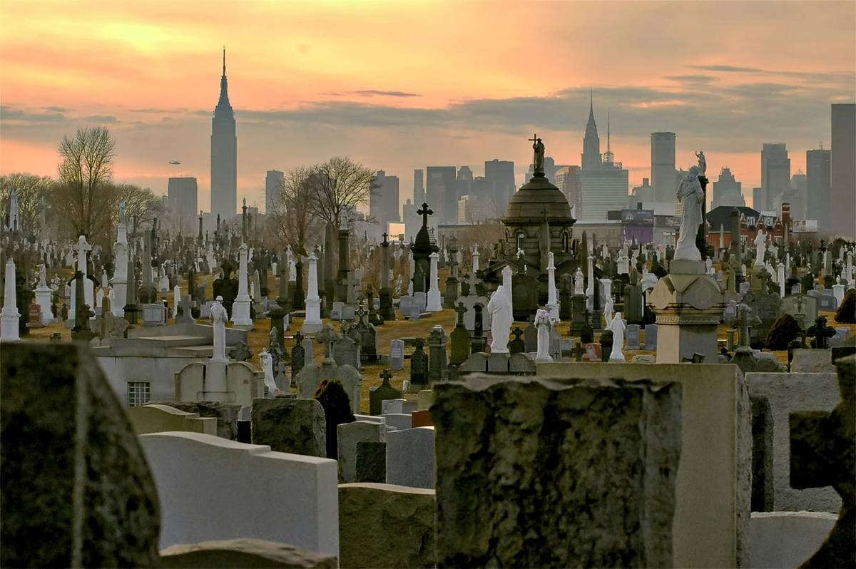 Rows of white headstones and crosses with the Manhattan skyline at dusk