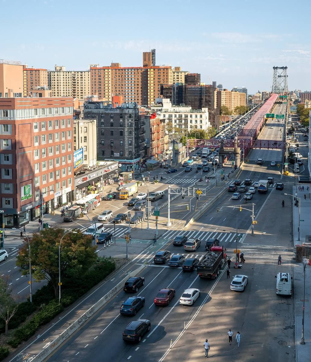 A broad street with traffic running towards a steel suspension bridge