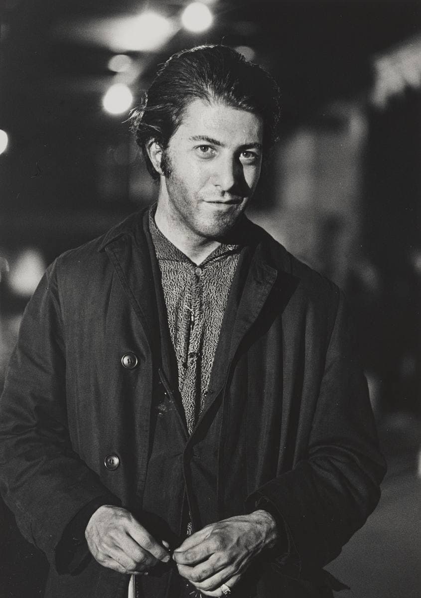 Dustin Hoffman, hair slicked back, in a dark jacket, at night on a city street