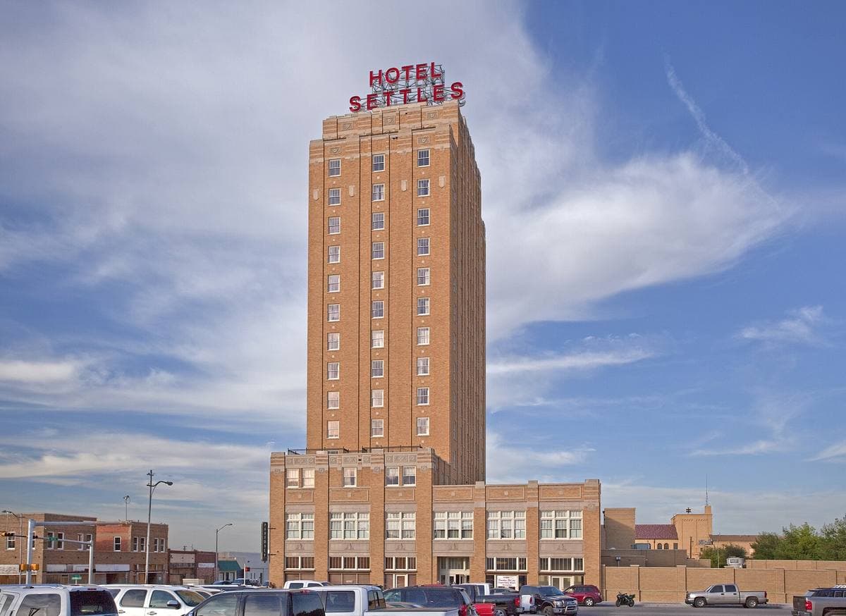 A fifteen-storey brick hotel tower with a red neon sign on its roof, blue sky