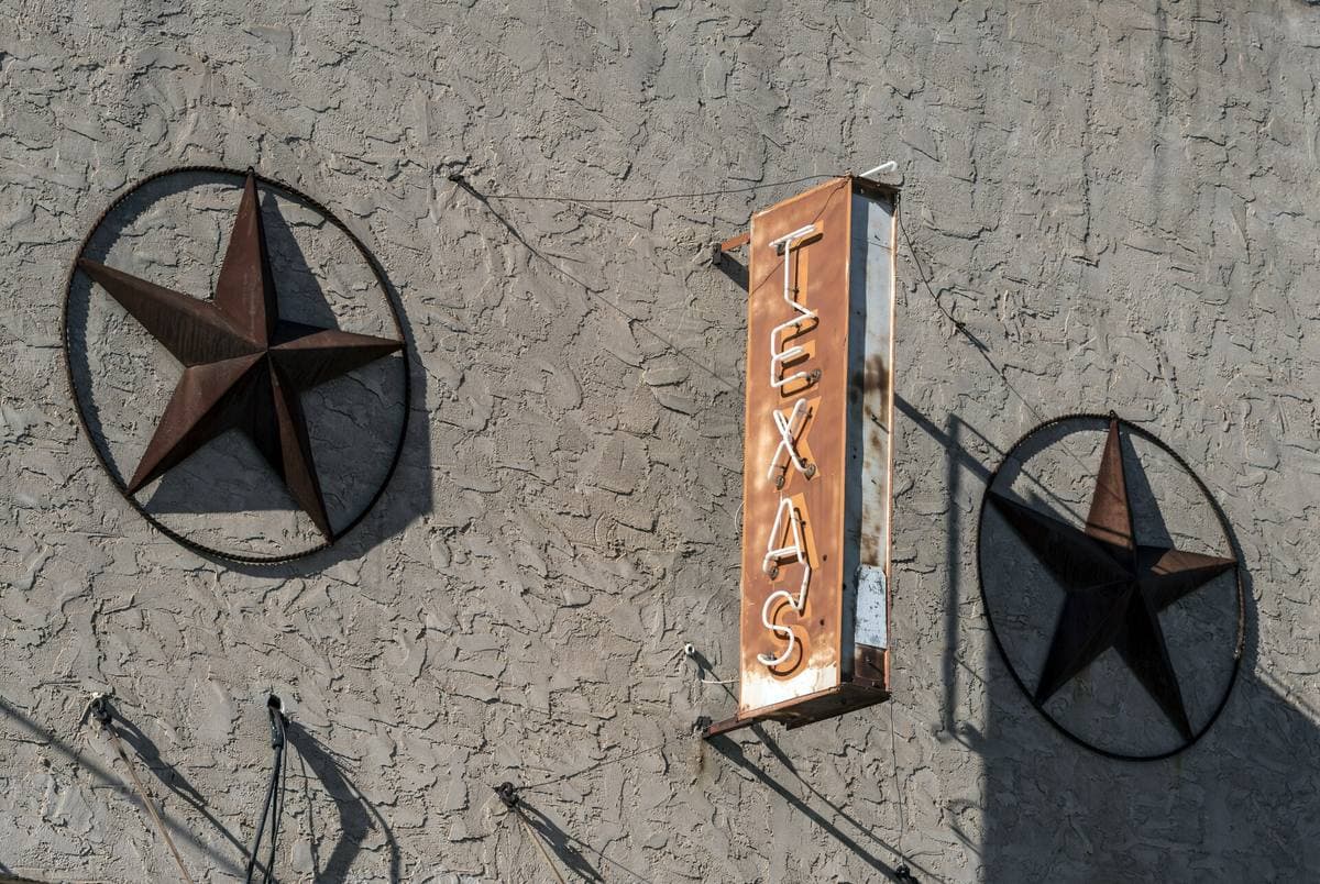 A vertical neon sign reading Texas between two iron stars on a white wall