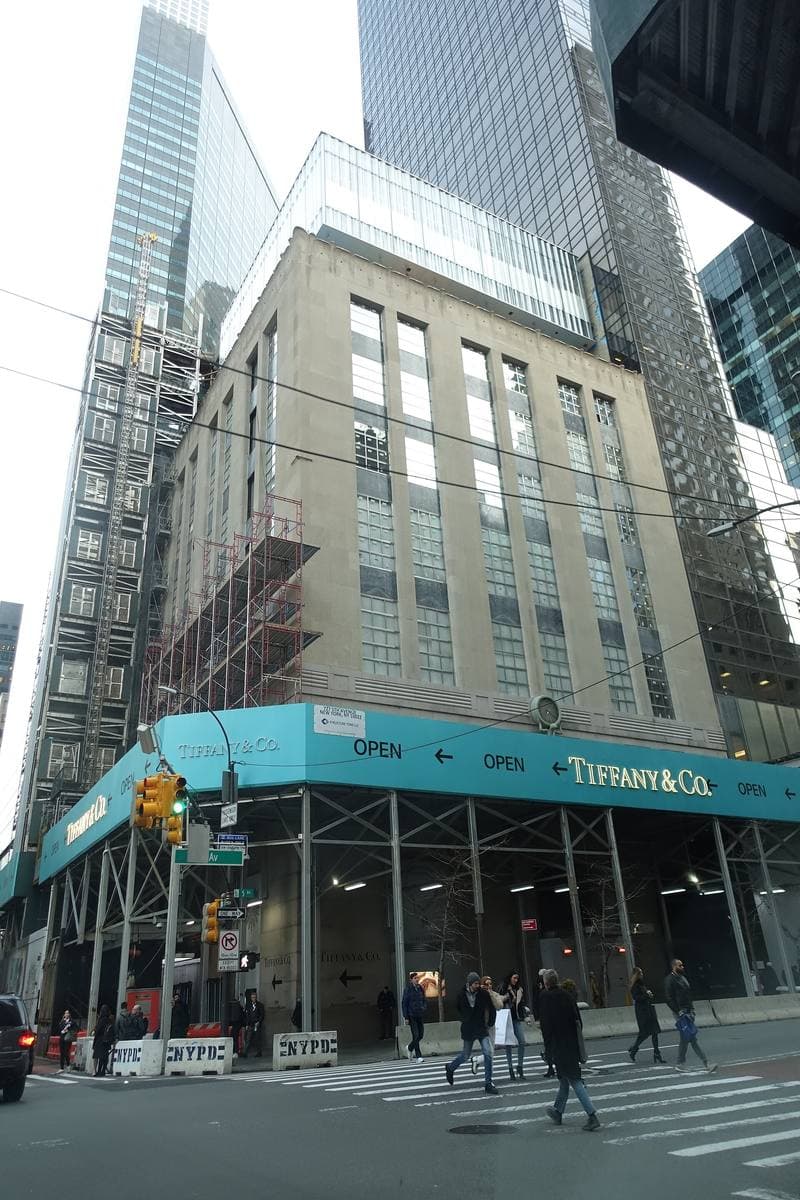A pale stone corner building on Fifth Avenue with a blue-green awning