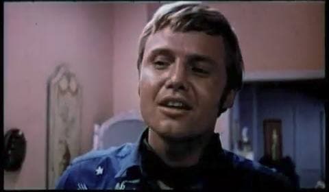 Jon Voight, fair hair, in a blue western shirt with white stars, talking