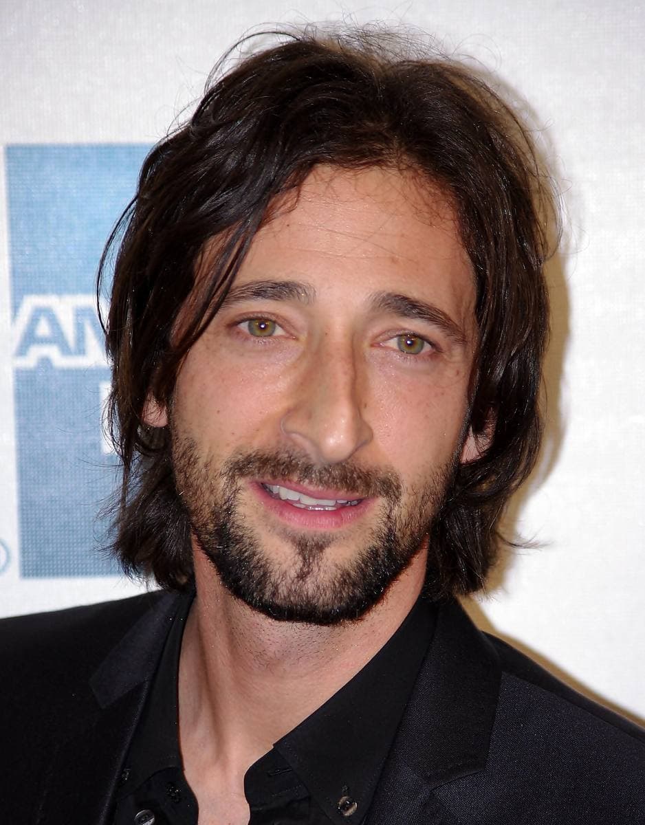 Adrien Brody smiling, with a beard and dark collar