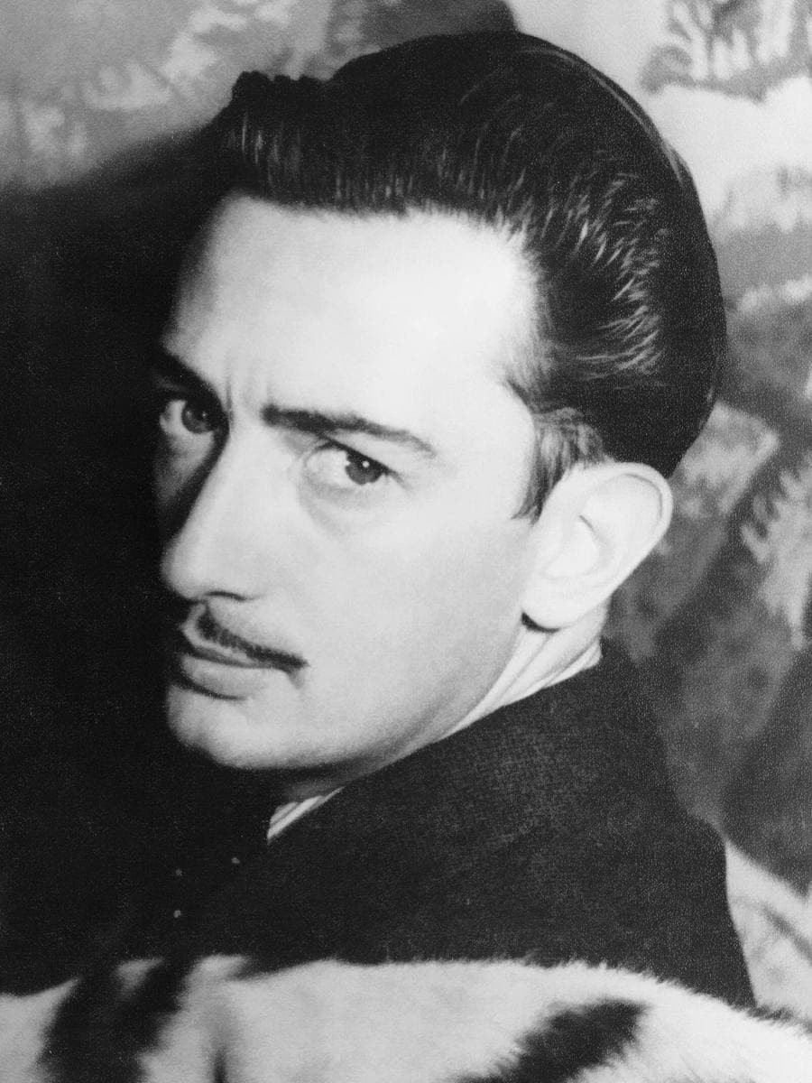 A black-and-white portrait of Salvador Dalí with a thin moustache and slicked hair, looking sideways