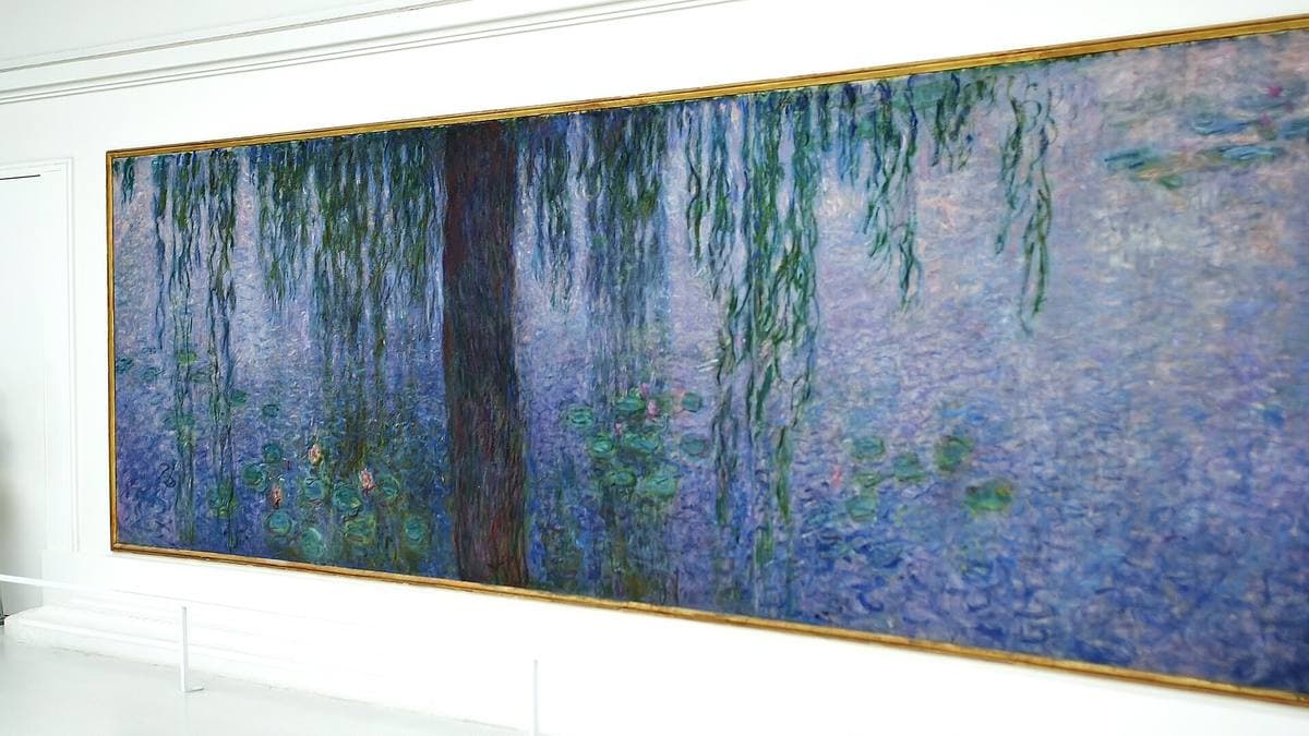 A long Monet water-lily canvas with willow trunks, hung on a white curved wall