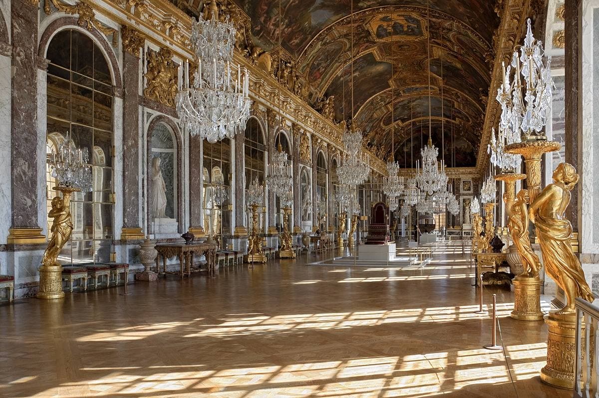 The Hall of Mirrors at Versailles, with chandeliers, gilded statues and sunlight on the parquet