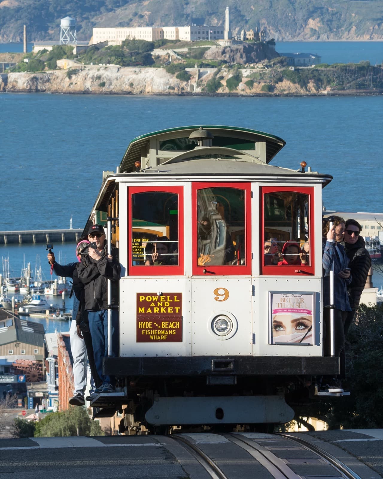 A red and cream cable car climbing Hyde Street with the bay and Alcatraz behind