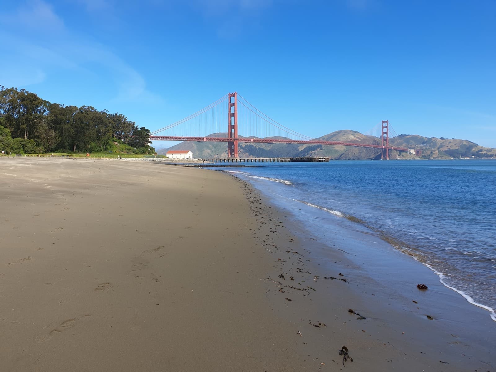 A sandy beach curving towards the Golden Gate Bridge under a blue sky