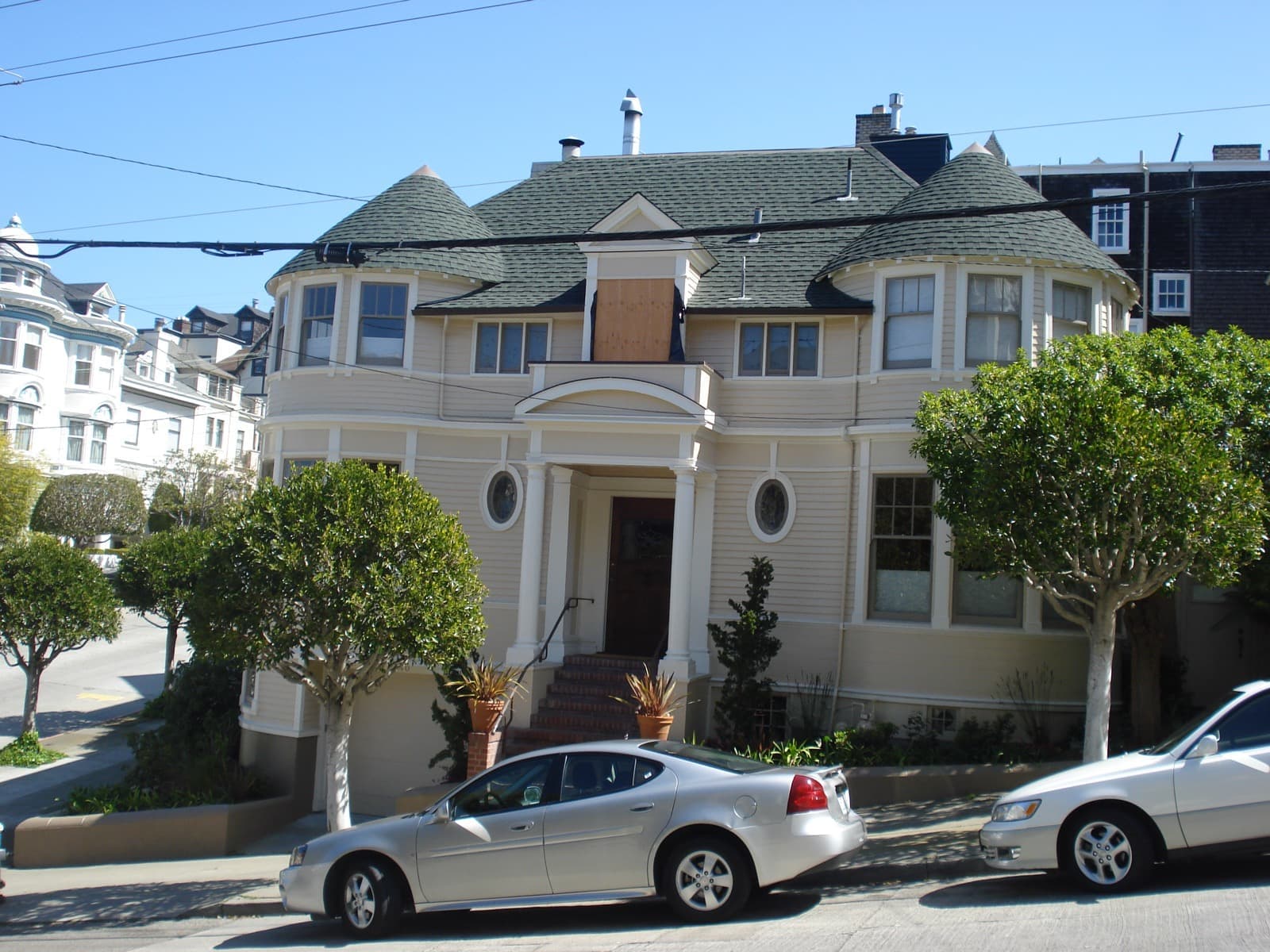 A pale yellow Victorian house with a pillared porch and bay windows on a corner in Pacific Heights