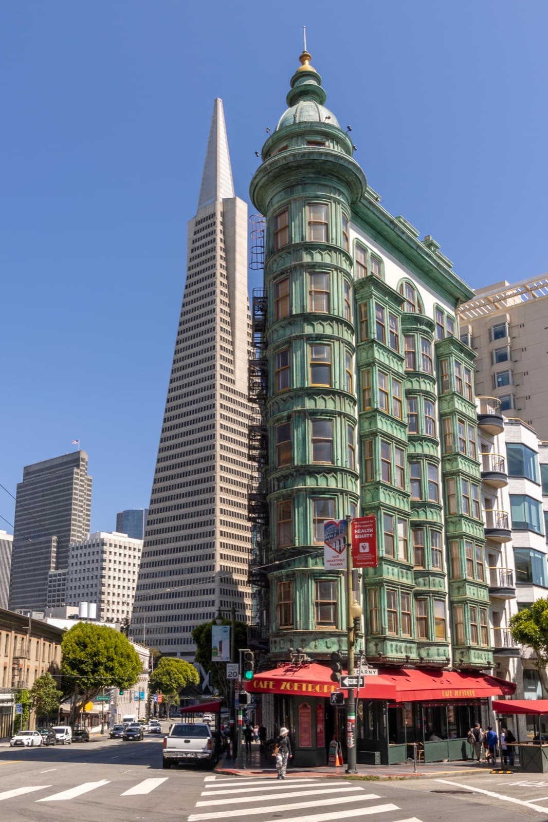 A narrow green copper-clad flatiron building with red awnings, the Transamerica Pyramid behind