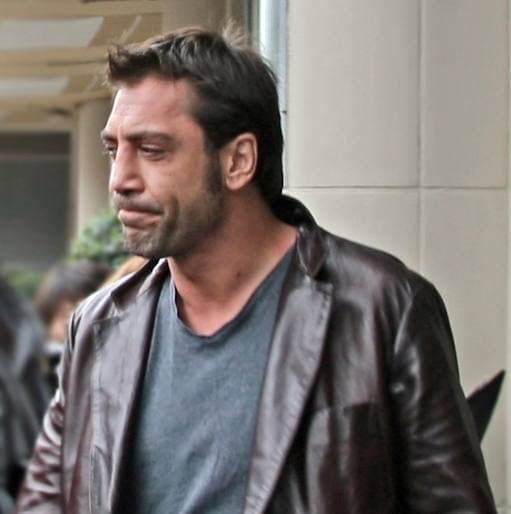 Javier Bardem in a peaked cap and dark jacket, smiling