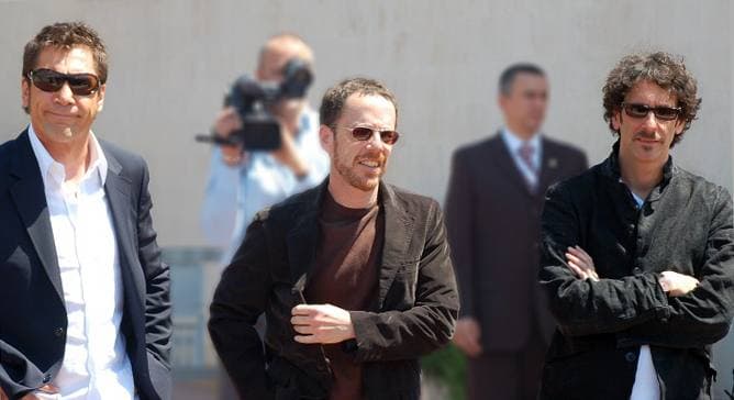 Javier Bardem in sunglasses and a white shirt beside Ethan and Joel Coen, outdoors